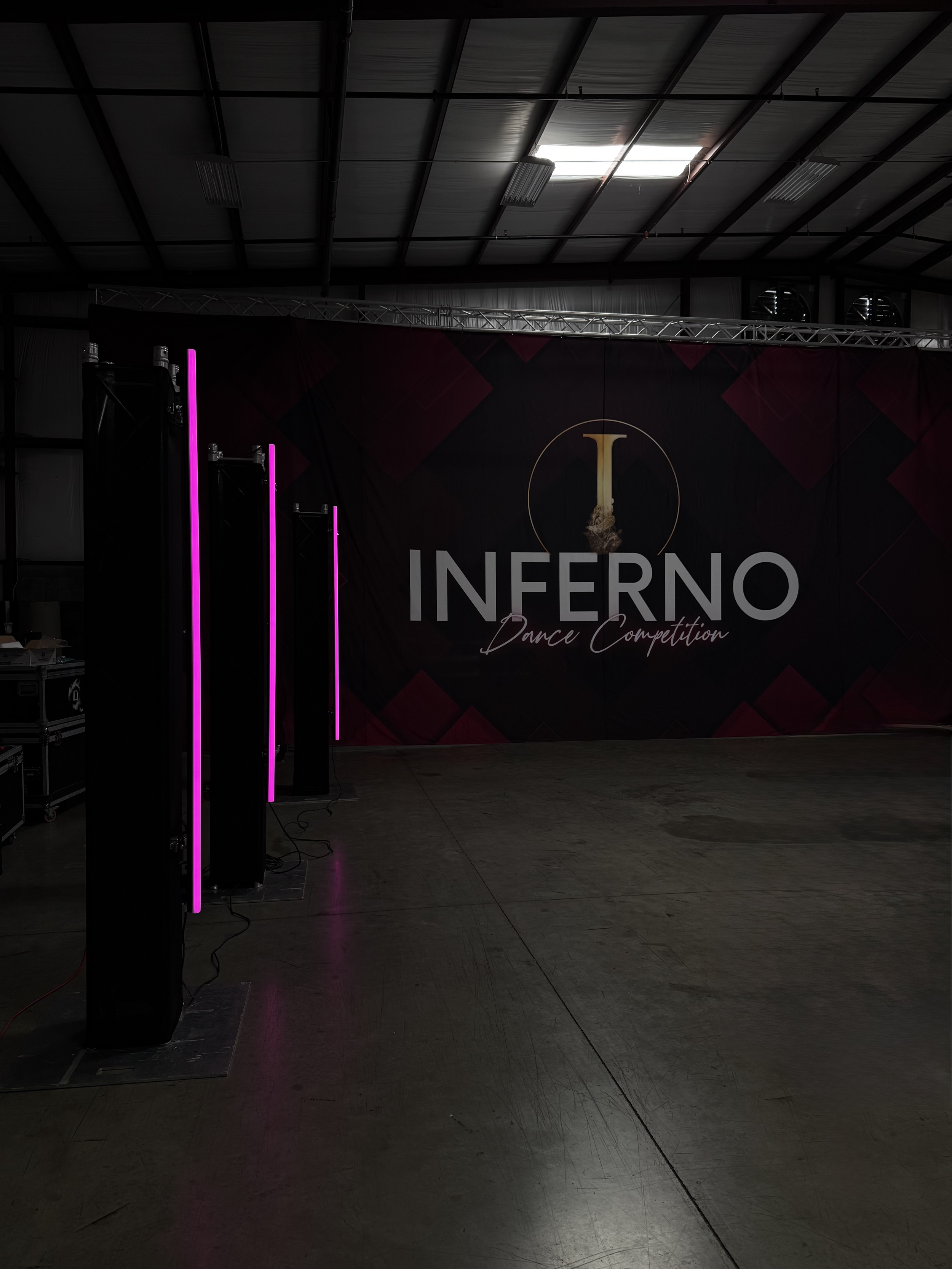 Dark indoor event space with a large banner reading 'Inferno Dance Competition' and vertical pink neon light installations on the left.