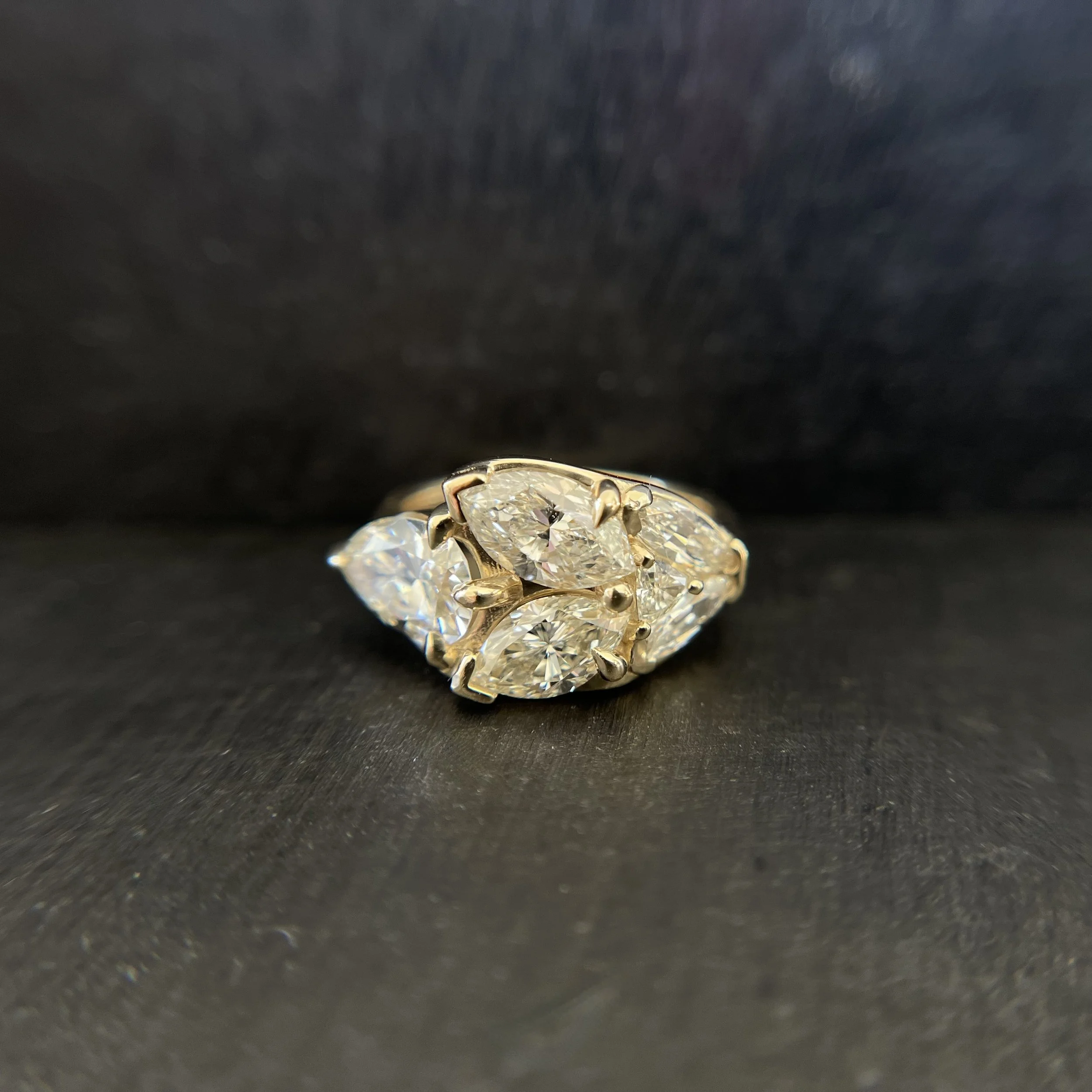 Gold ring with multiple large diamonds set in a prong setting, displayed on a black surface.