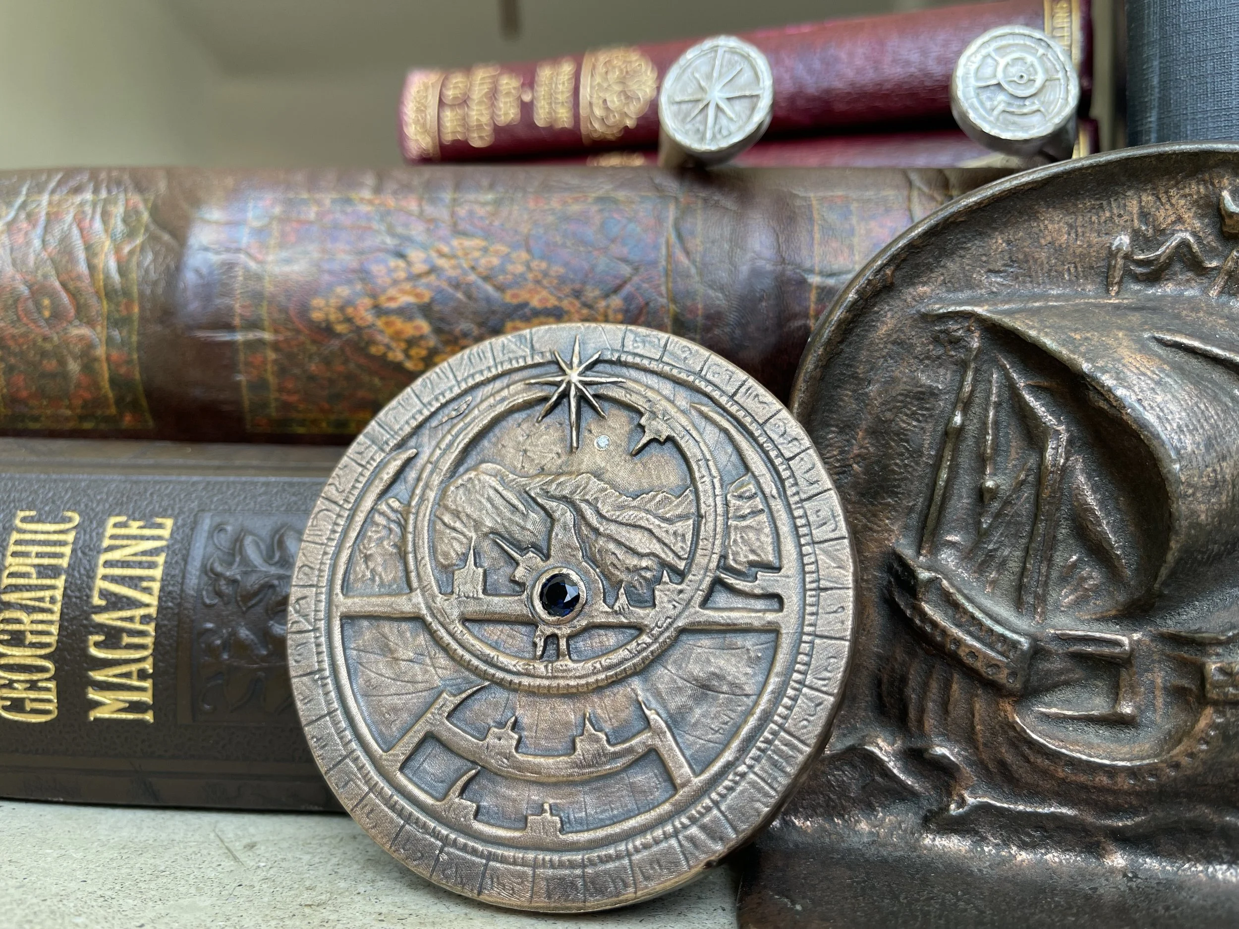 Close-up of vintage looking metal medals and trophies on a bookshelf, including a circular medal with mountain and star design, a bronze medal with a military emblem, and books with gold and red spine details.