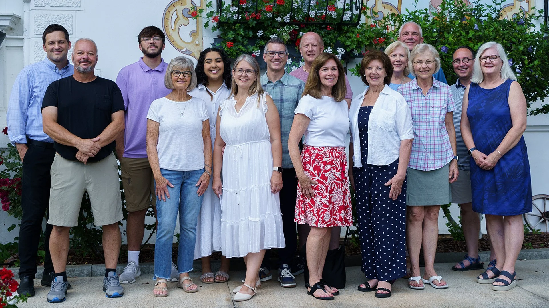 Group of people posing outdoors in front of a decorated wall with flowers.