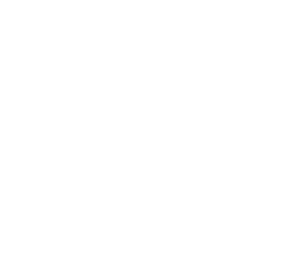 A light-colored dog sitting on grass in front of a building with people walking nearby.