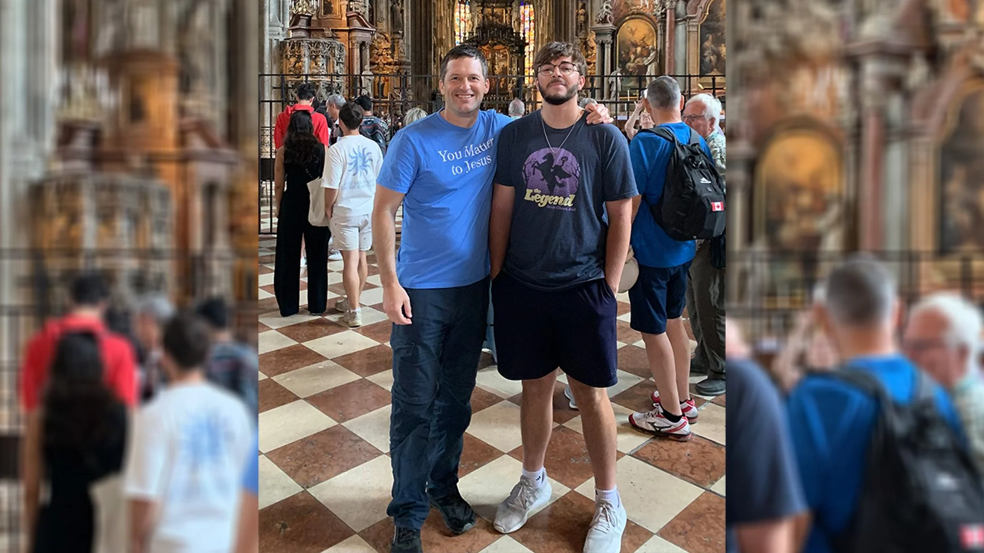 Two men standing and smiling inside a church with a crowd of people in the background.