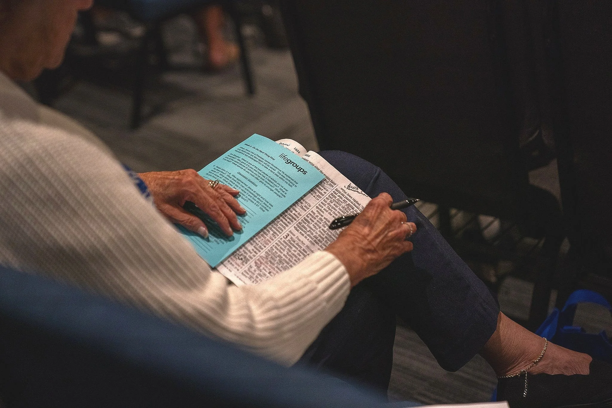 An elderly person sitting in a chair, reading a pamphlet and taking notes during a conference or seminar.