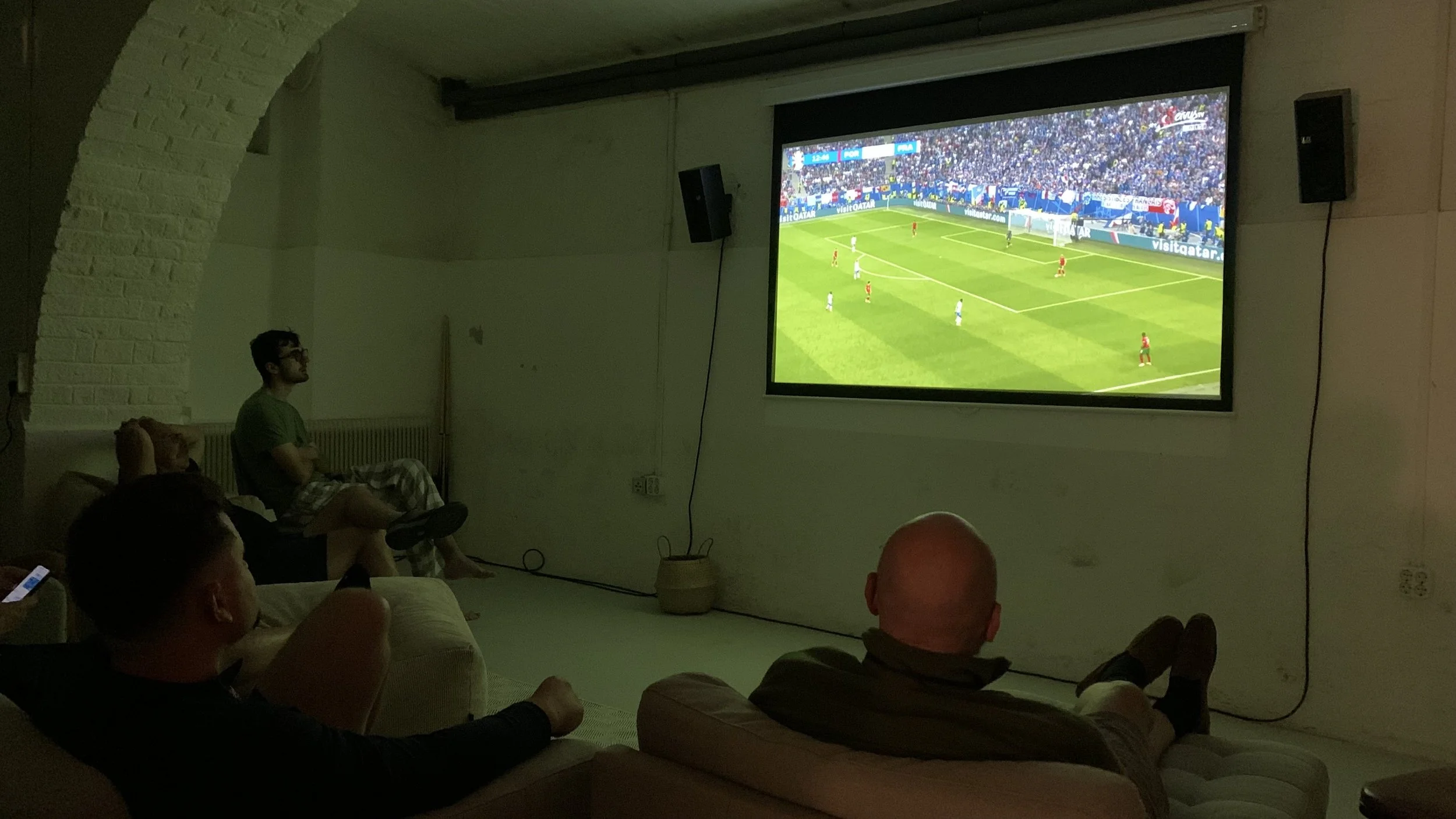 People watching a soccer game on a large screen in a dark room.