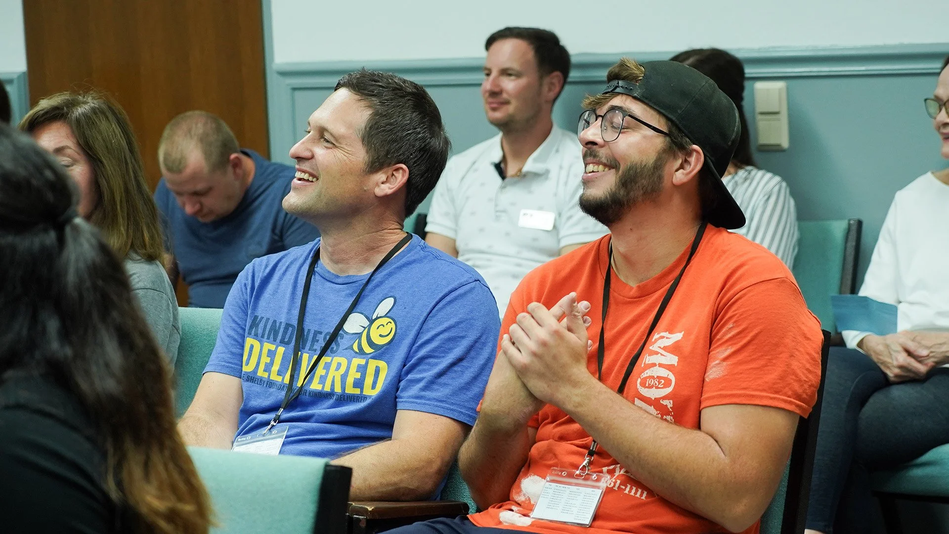 People sitting in a room at a conference or seminar, smiling and enjoying the event.