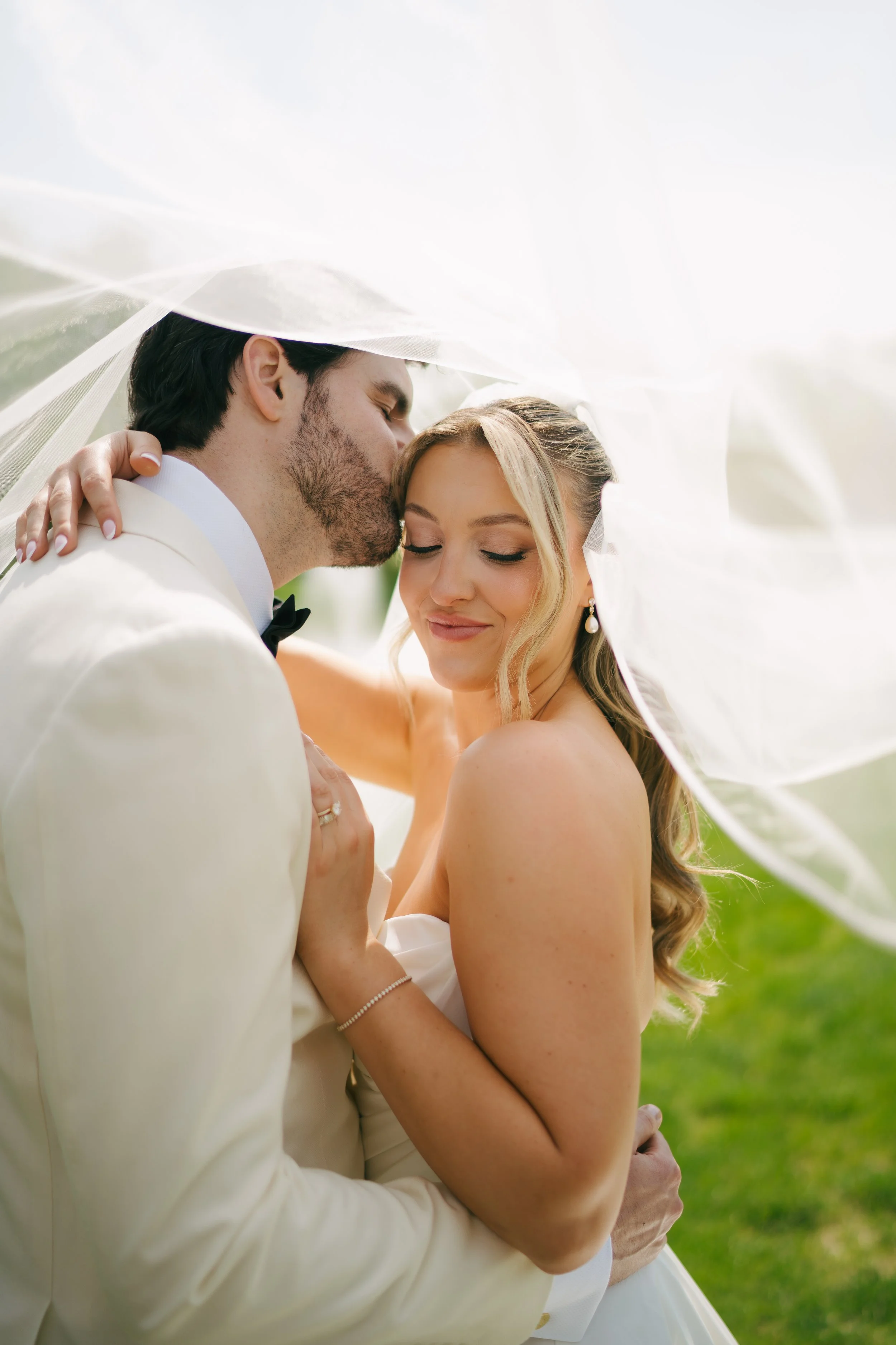 Newlywed couple embracing beneath a white wedding veil outdoors