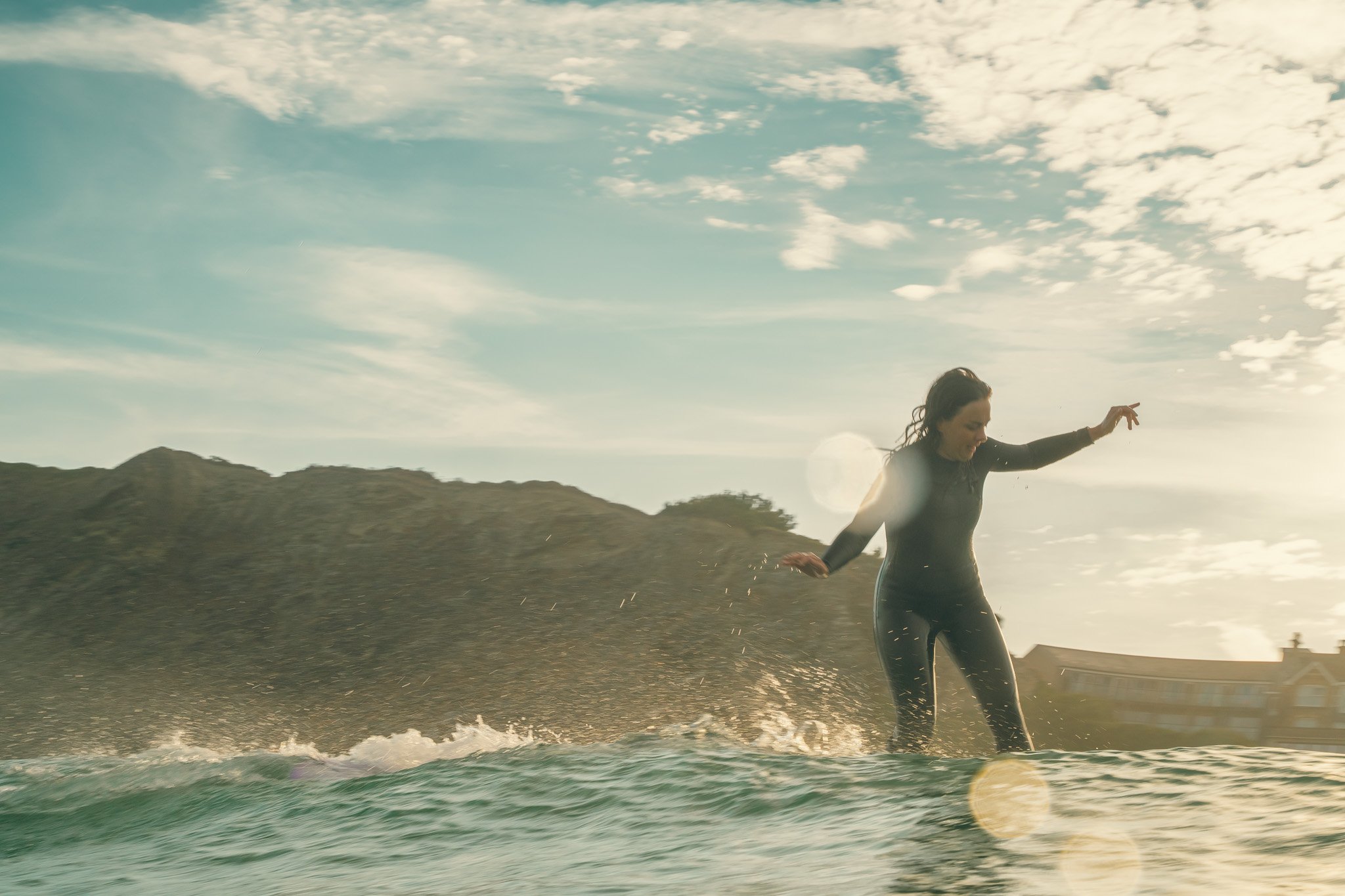 Georgie gliding past the surf photographer on a beautifully backlit wave during a golden summer dawn surf session at Watergate Bay, Newquay, Cornwall.
