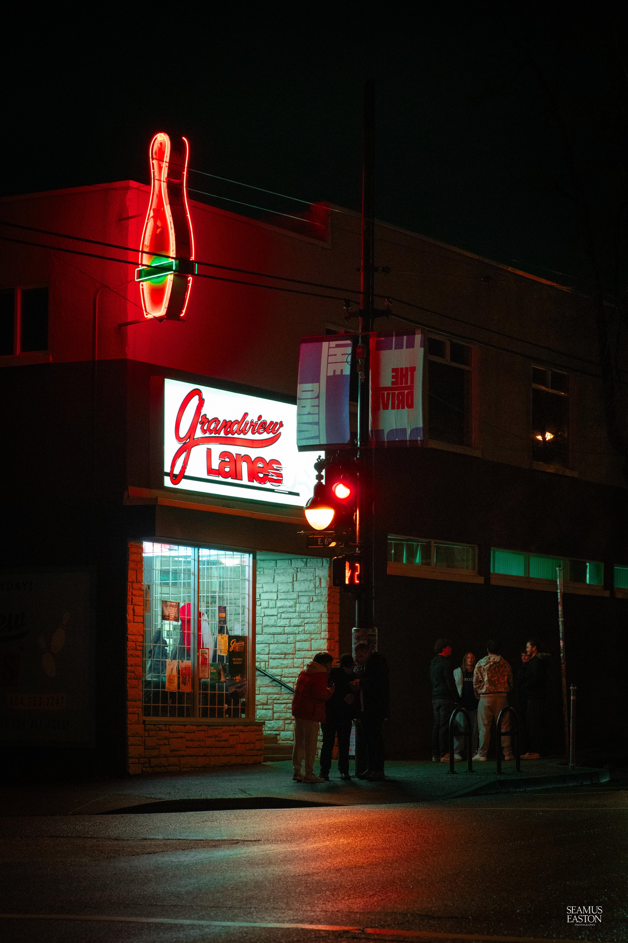 Night view of Grandview Lanes bowling alley with neon signs, and people standing outside on the sidewalk.