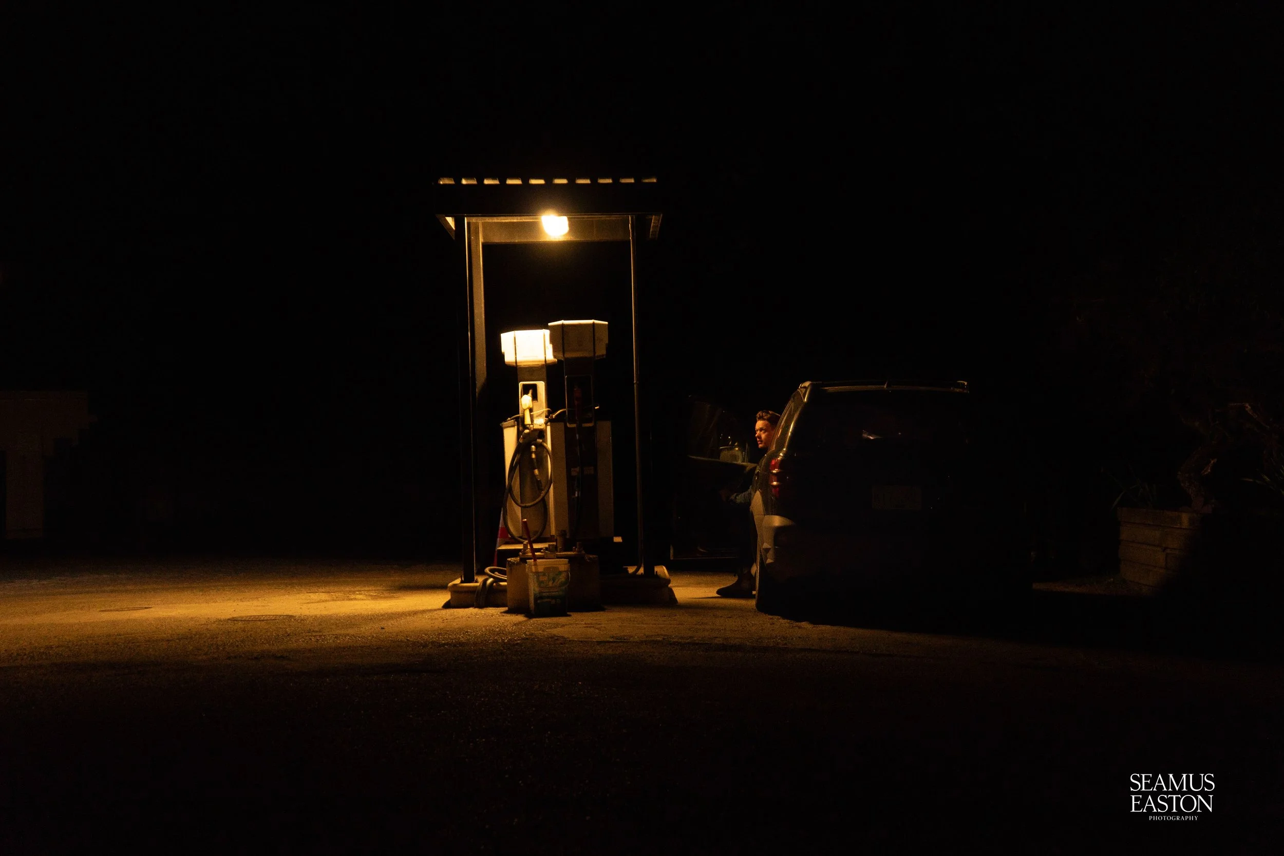 A dimly lit gas station at night with a person sitting in a car next to the pumping station.