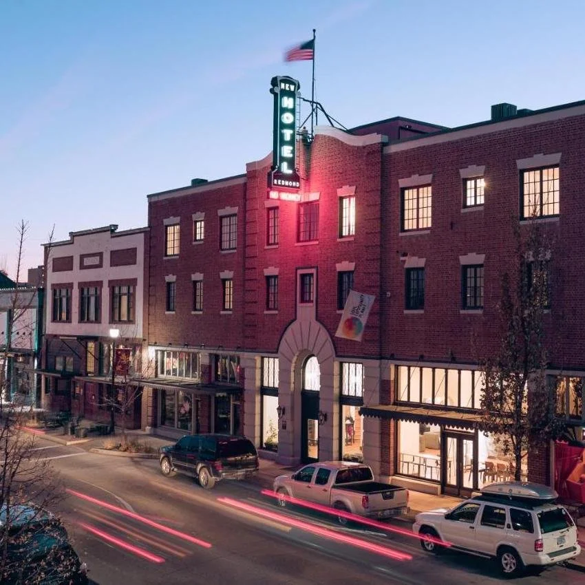 Historic SCP Redmond Hotel building illuminated at dusk in downtown Redmond, Oregon, with its vintage neon sign and cars along the street.