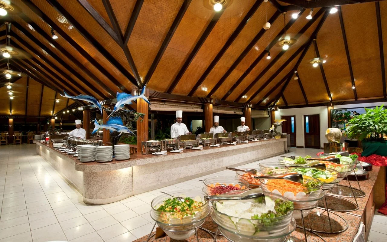 Fresh salads and vegetables displayed at a buffet inside an open-air tropical resort restaurant.