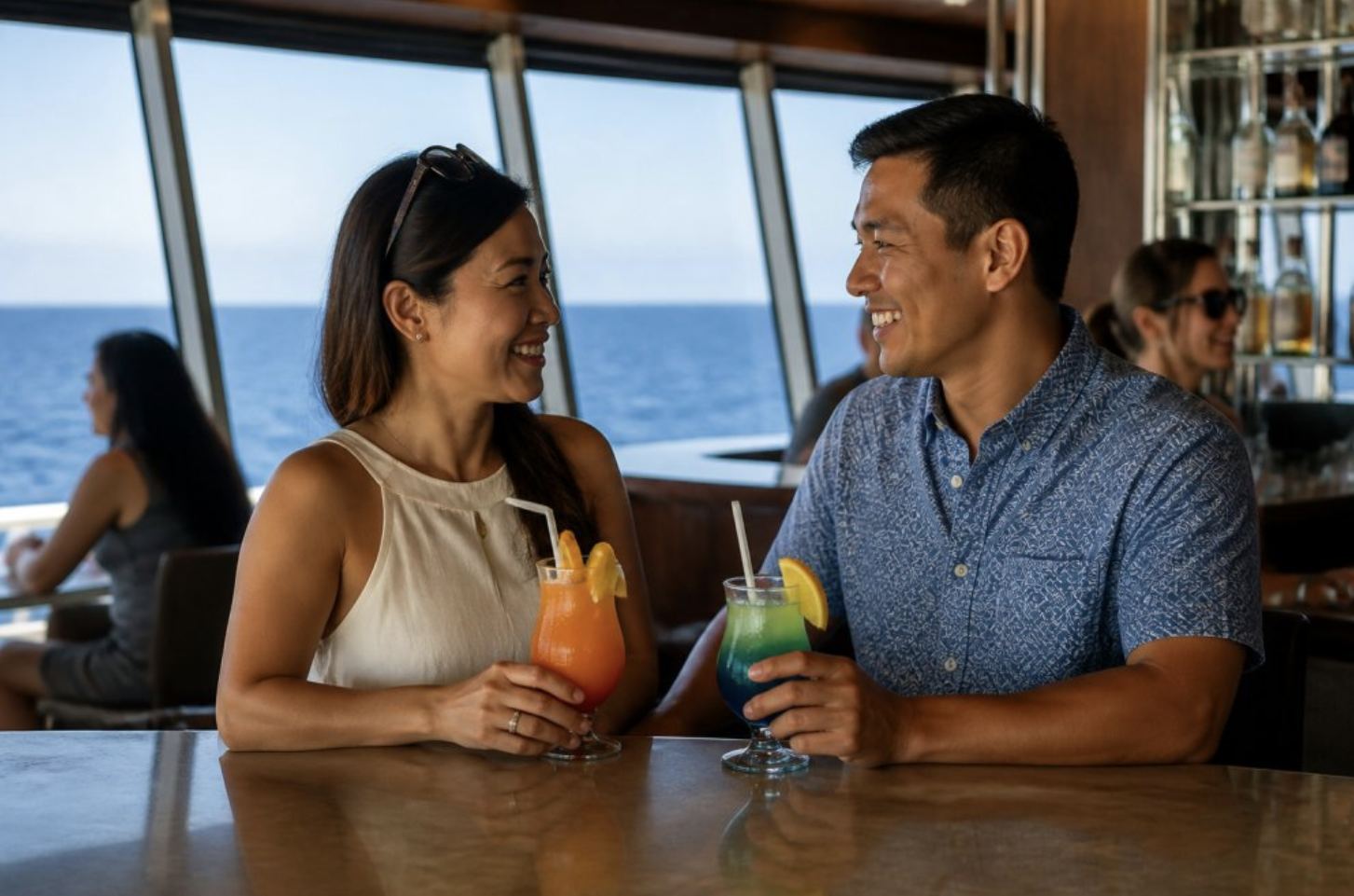 A smiling couple enjoys colorful tropical cocktails together at a cruise ship bar overlooking the ocean.