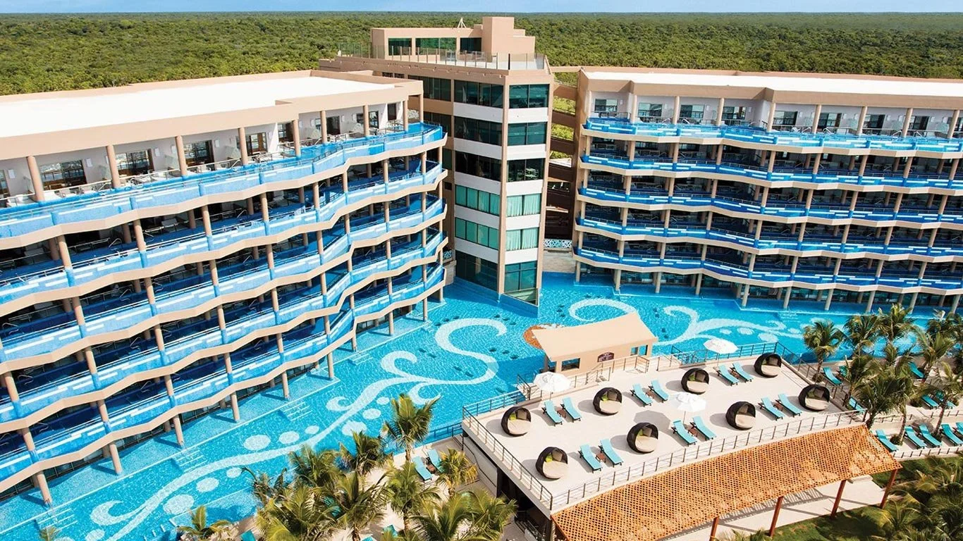 Aerial view of a modern luxury resort with swim-out suites, private balconies, a large winding pool, and rooftop lounge chairs.