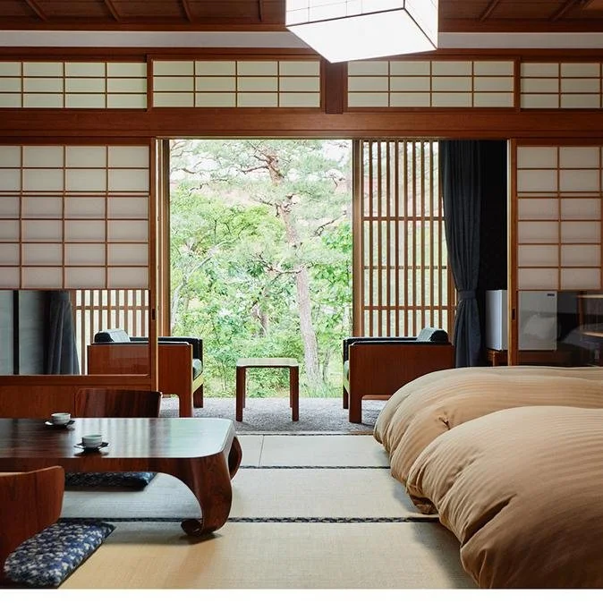 A traditional Japanese ryokan room with tatami flooring, futon bedding, and a peaceful garden view