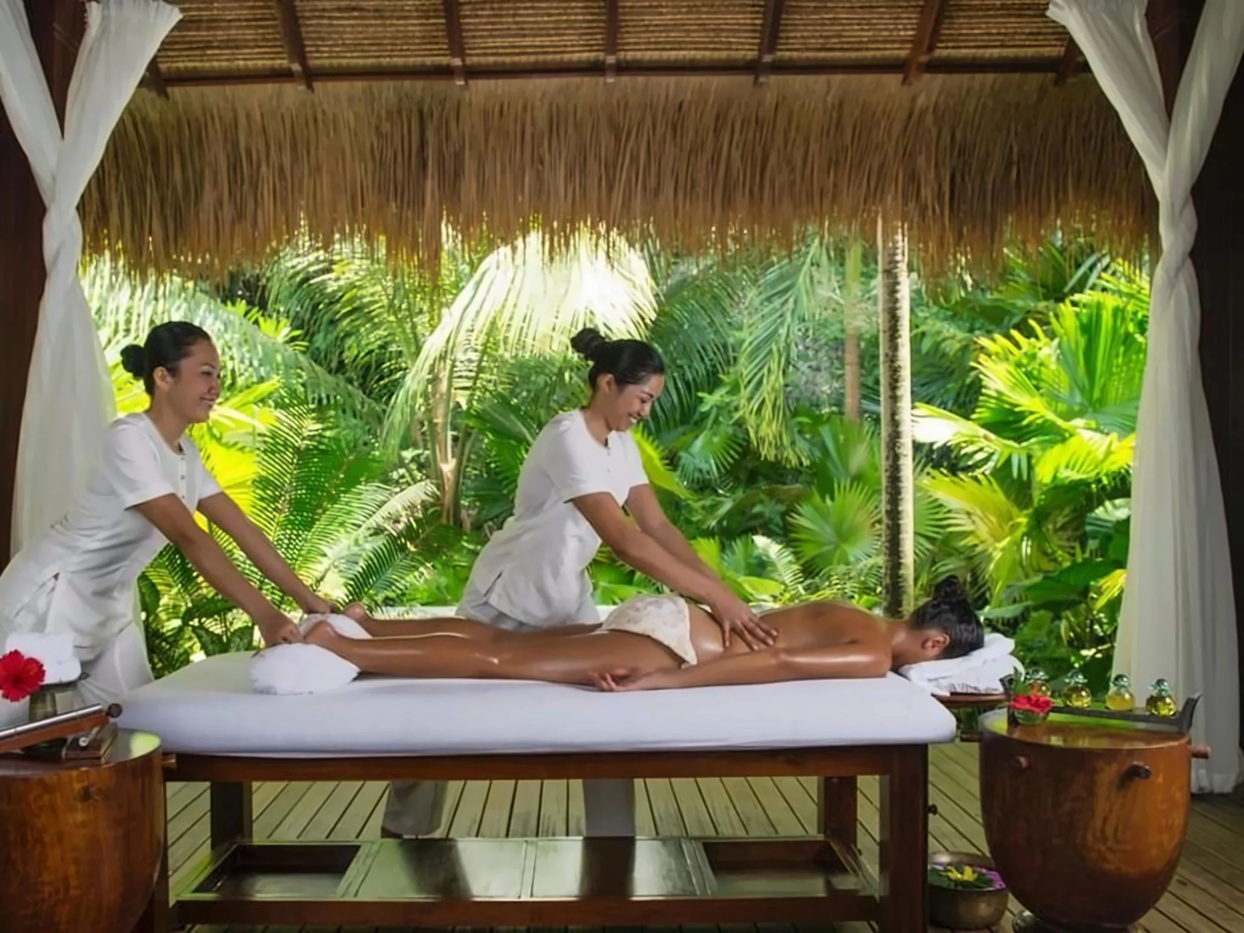 Guest enjoying an outdoor massage in a peaceful, thatched-roof spa pavilion surrounded by tropical greenery.