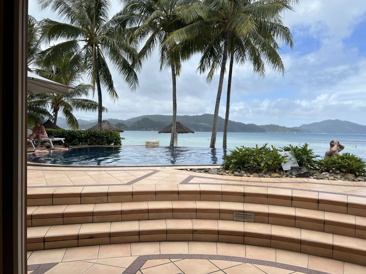Infinity pool lined with palm trees overlooking the turquoise ocean and lush islands at a Hamilton Island resort in the Whitsundays.