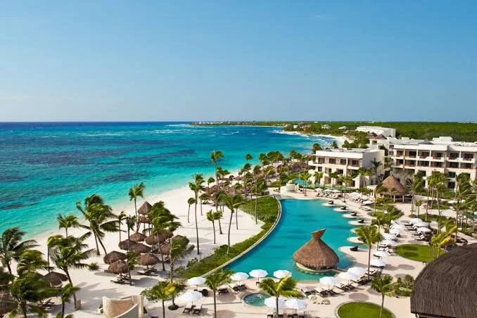 Aerial view of a Secrets adults-only resort featuring a beachfront pool, palm trees, lounge chairs, and turquoise Caribbean water.