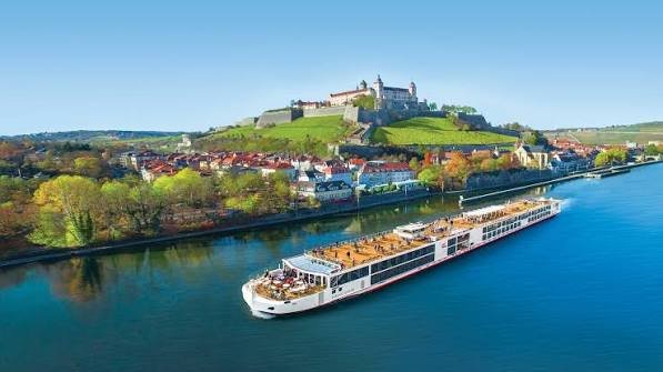 A river with a cruise ship sailing near a hillside town with a castle on top