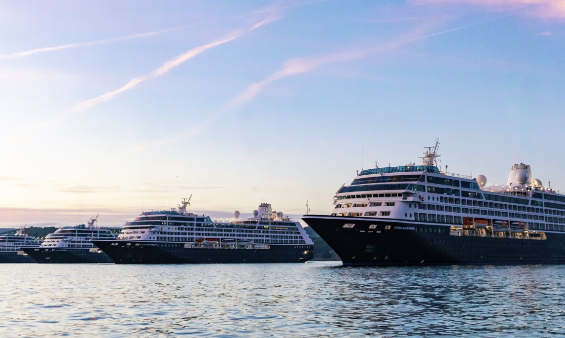 Azamara cruise ships docked together on calm water beneath a pastel sunset sky.