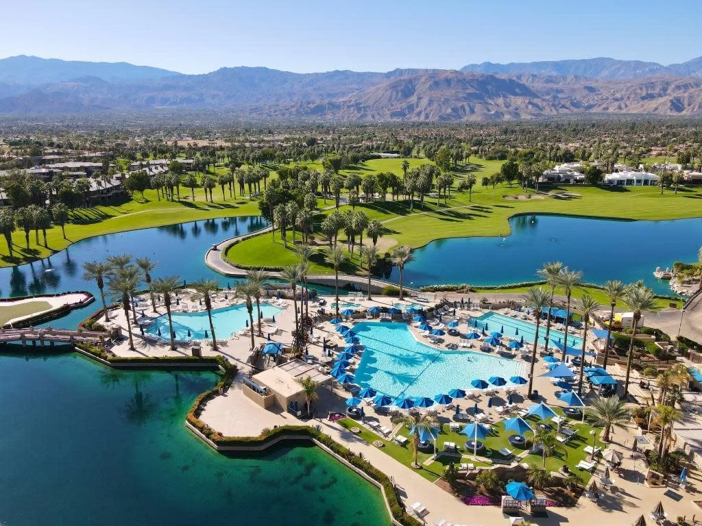 Palm-lined resort pool with a golf course and mountains in the distance.