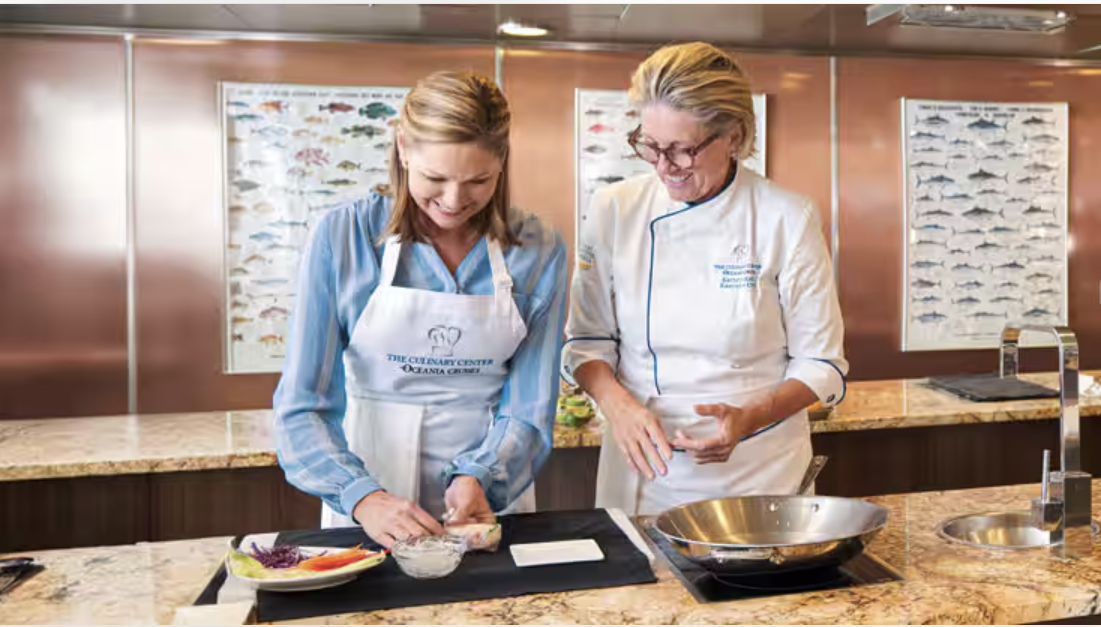 Guest wearing an apron prepares food beside a chef instructor in Oceania Cruises’ Culinary Center.