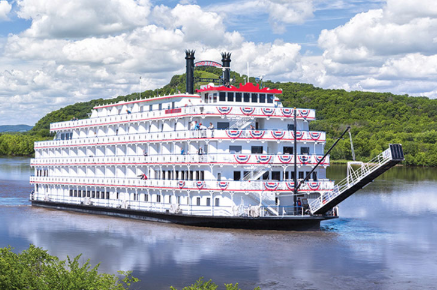 A large white river cruise ship decorated with red, white, and blue bunting on a calm river