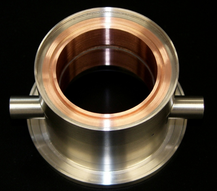 Close-up of a metallic circular mechanical component with a copper-colored interior and two small protruding rods on the sides, set against a black background.