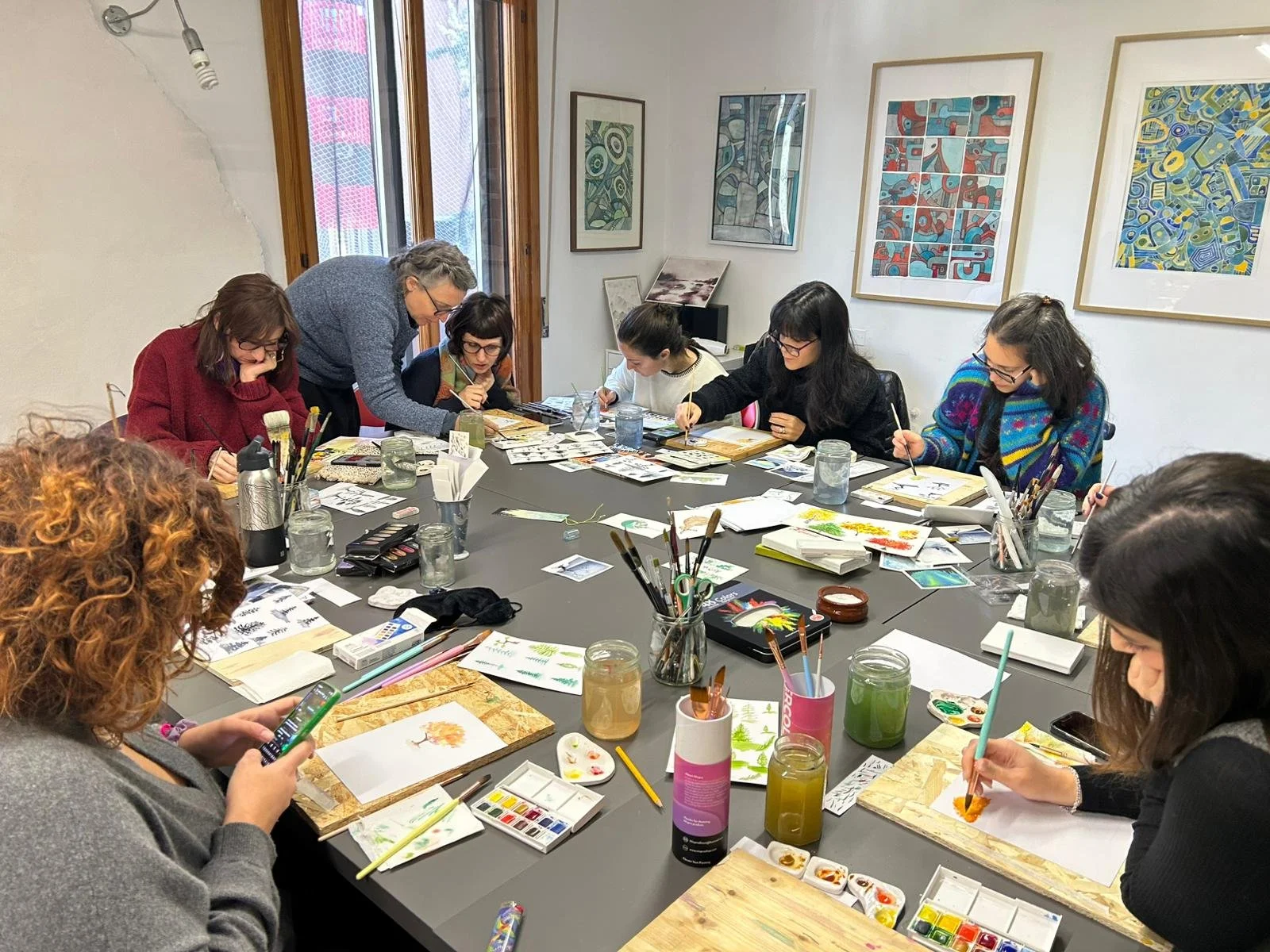 A set of watercolor paint containers filled with various shades of green, blue, black, and white, with some paint smeared around them.