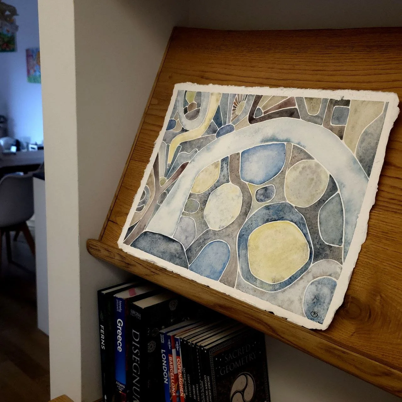 Watercolor painting of an abstract geometric spiral design with green, blue, and brown shades on a white paper.