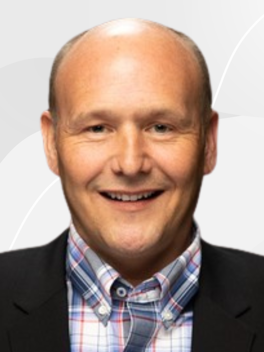 Headshot of a smiling man with a bald head, wearing a dark blazer and a multicolored plaid shirt.