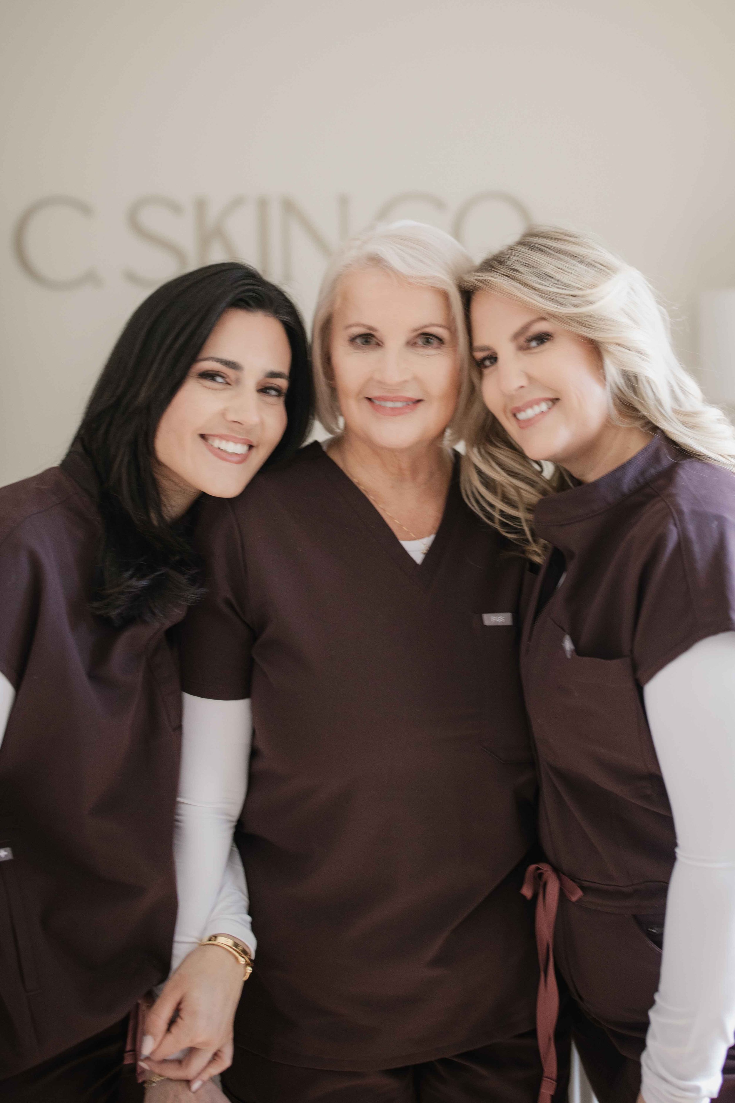 Three women in brown uniforms smiling indoors.