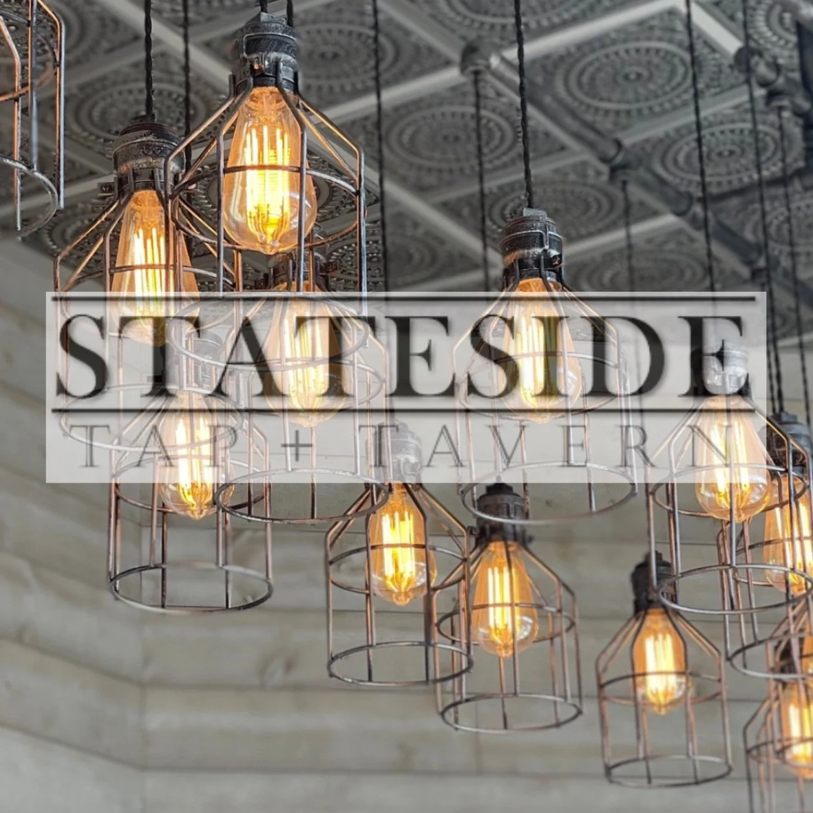 Industrial-style chandelier with multiple Edison bulbs hanging from a decorative ceiling.