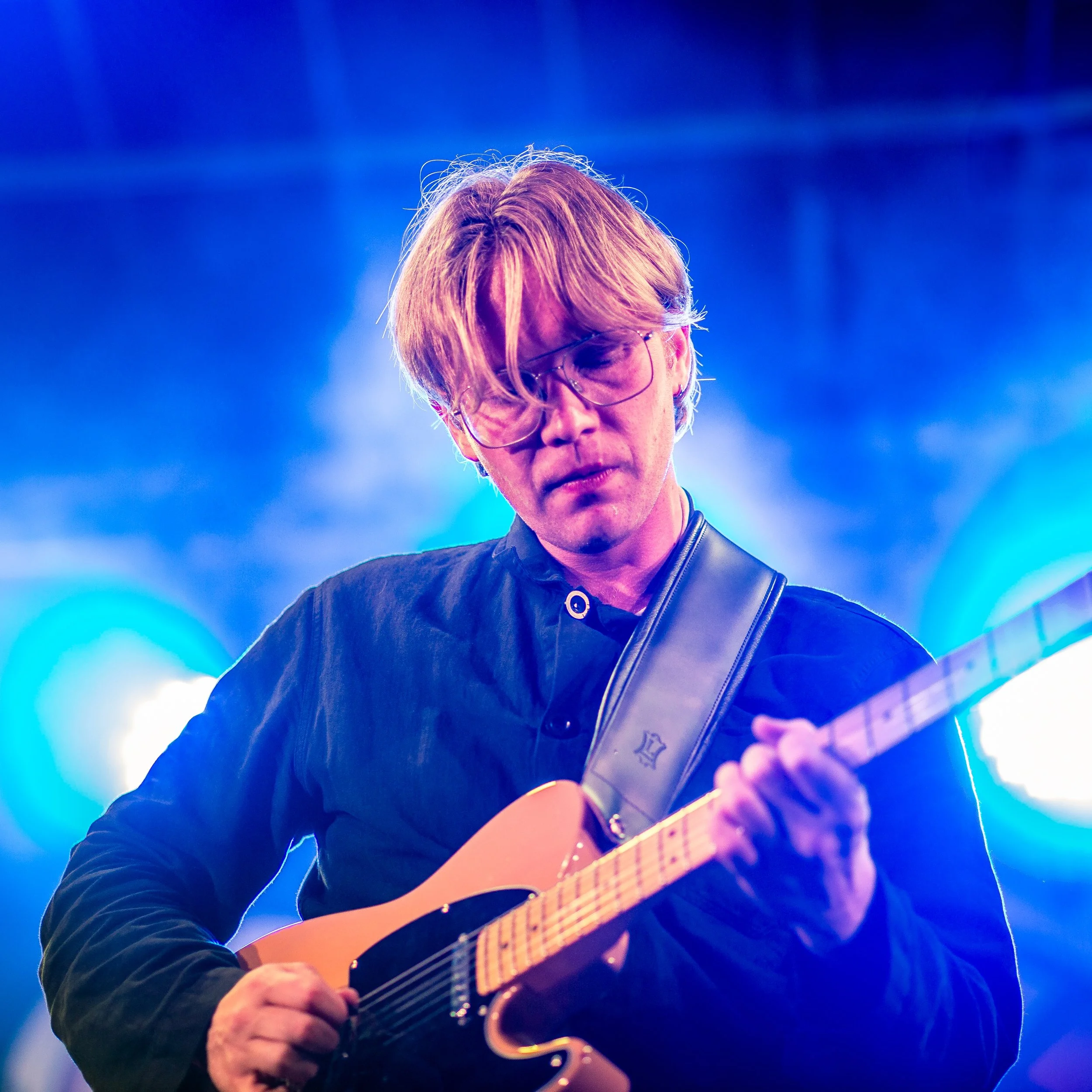 A man playing an electric guitar during a live performance, illuminated by stage lights.