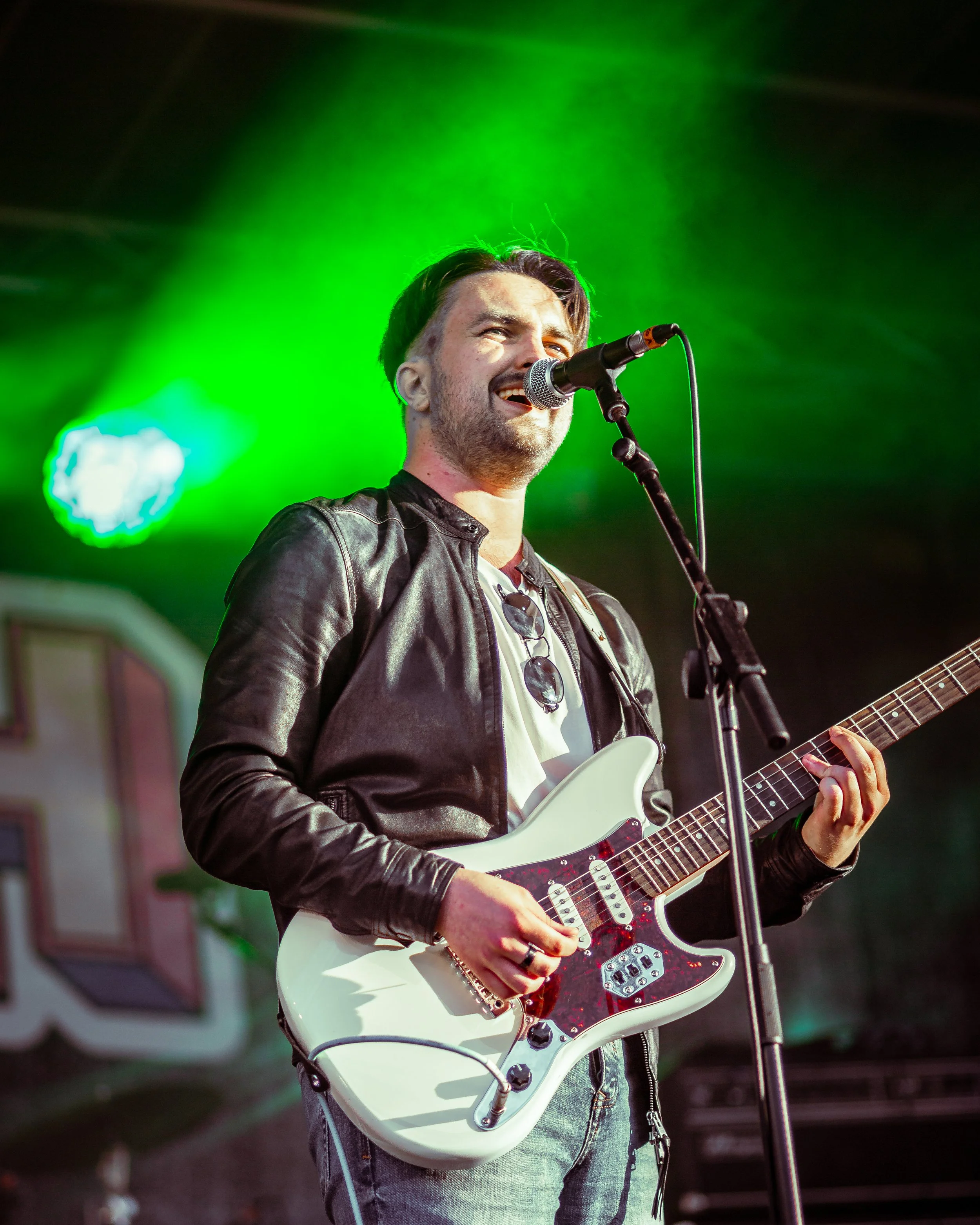 A man singing into a microphone while playing an electric guitar on stage with green lighting