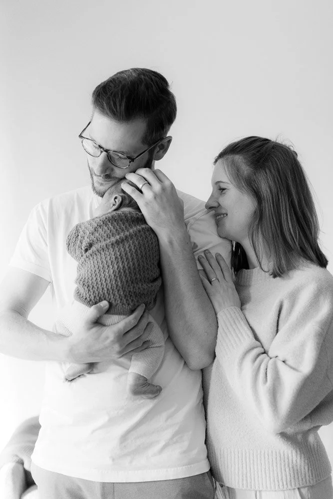 Eltern mit Baby auf dem Arm, kuscheln und lächeln das Baby an