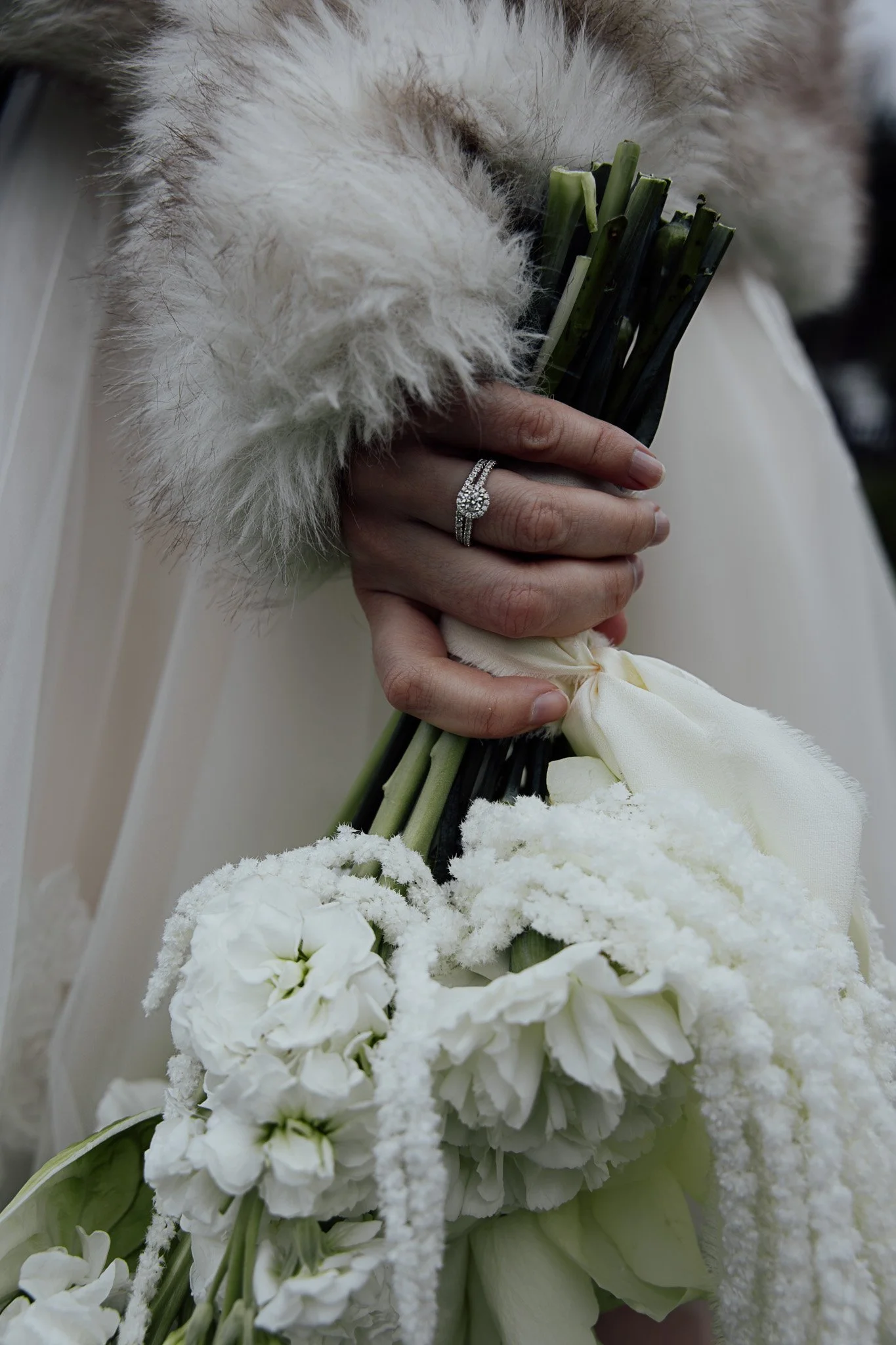 Bride holding a white wedding bouquet featuring textured seasonal blooms and soft foliage.