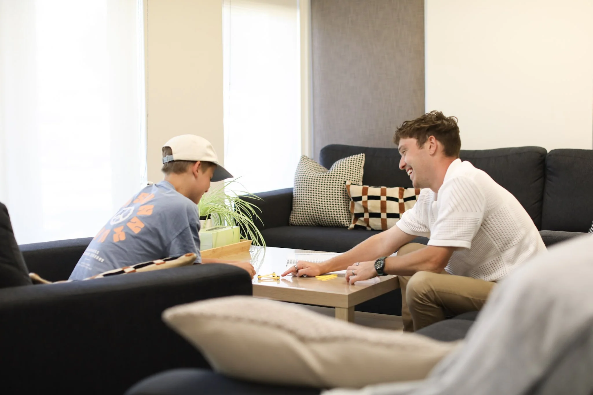 Two people sitting on a black couch, playing a game together at a coffee table, smiling and having fun.