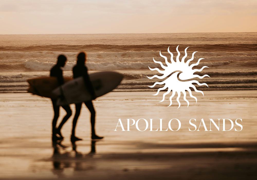 Two surfers walking on the beach at sunset, carrying surfboards, with the logo and text 'APOLLO SANDS' overlayed.