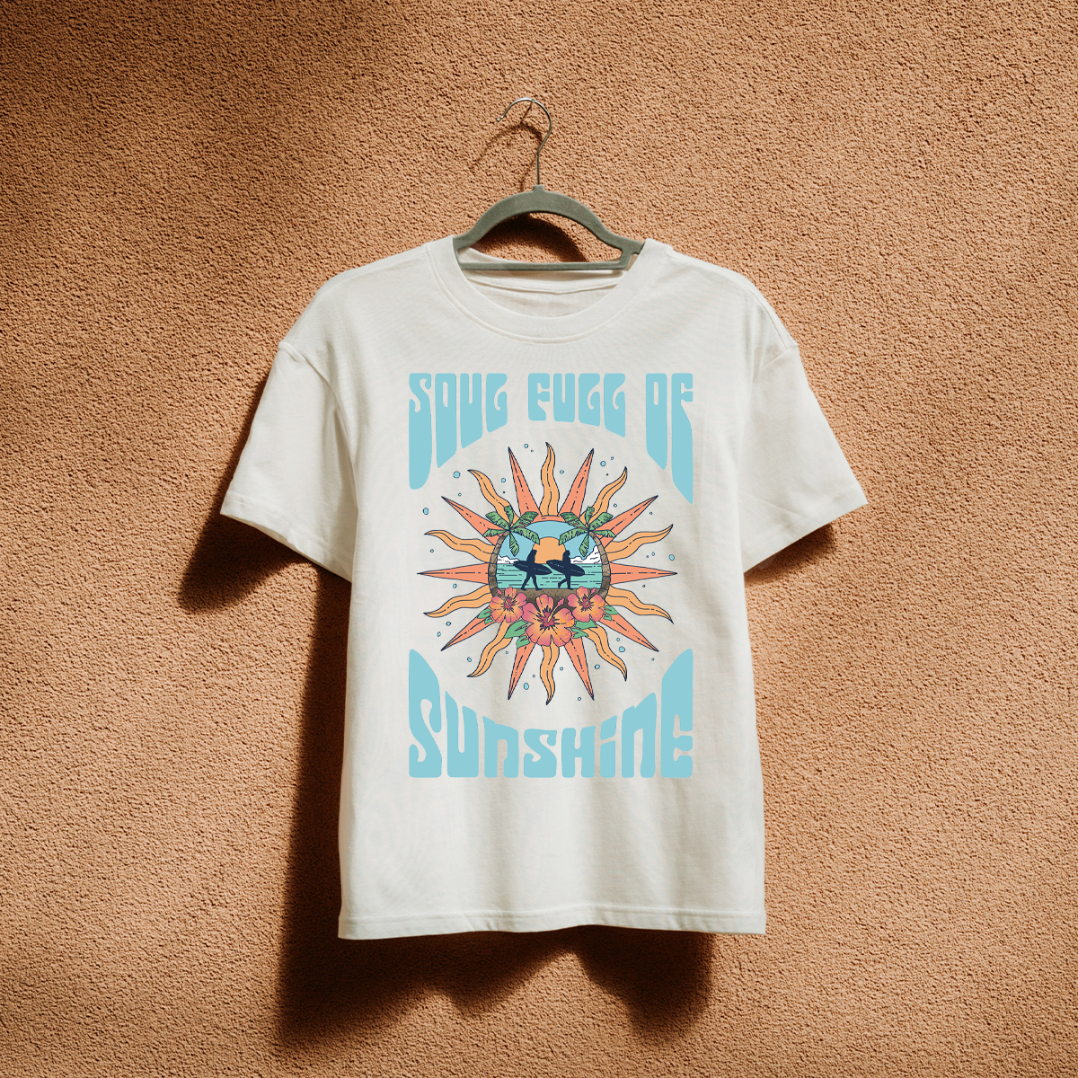 White T-shirt hanging on a hanger with a colorful tropical design featuring the text 'SOG EGG OF SUNSHINE', surrounded by a sun, palm trees, flowers, and a sun at sunset scene.