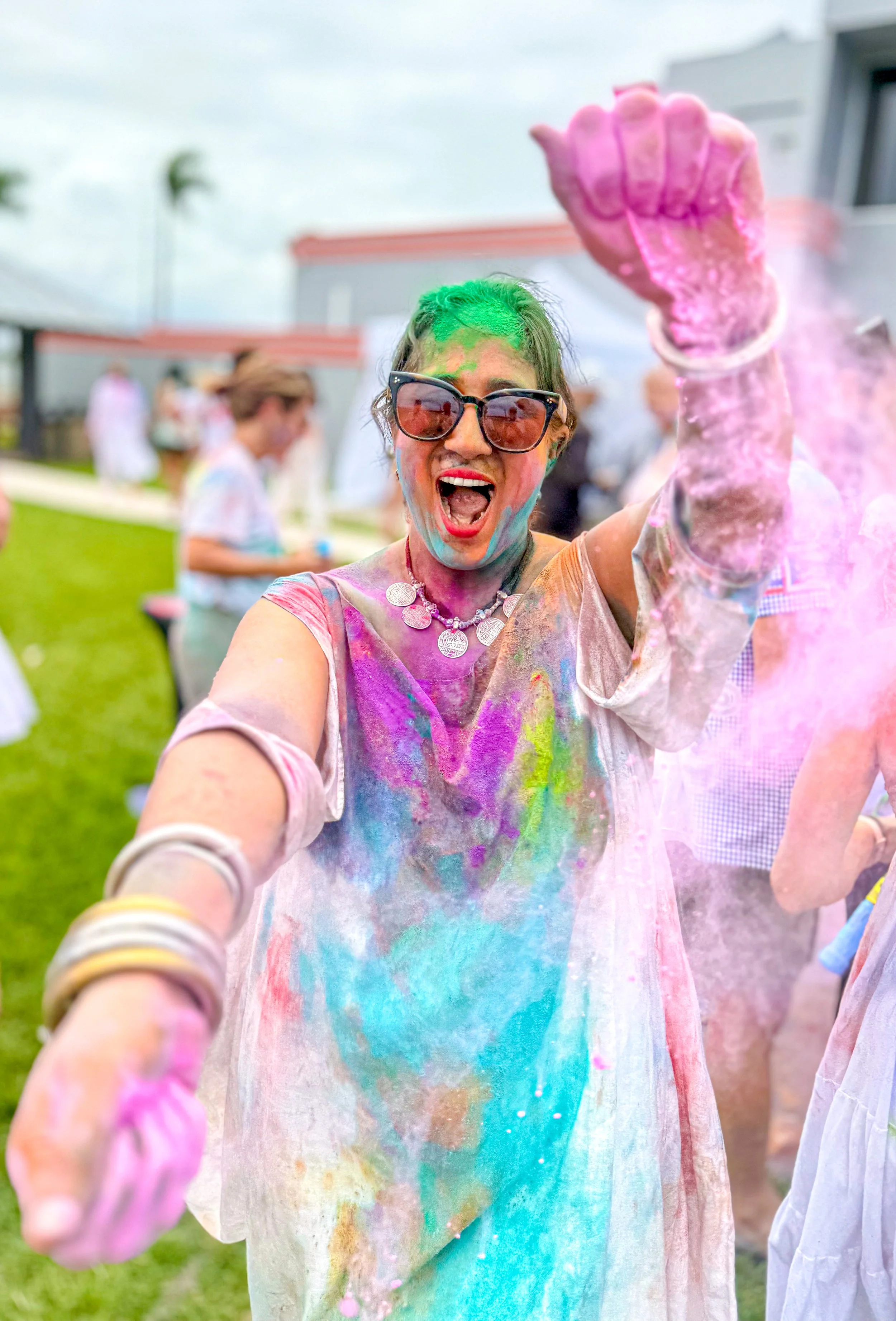 Woman celebrating at a colorful outdoor event, throwing pink powder, her face and clothes covered in vibrant colors.