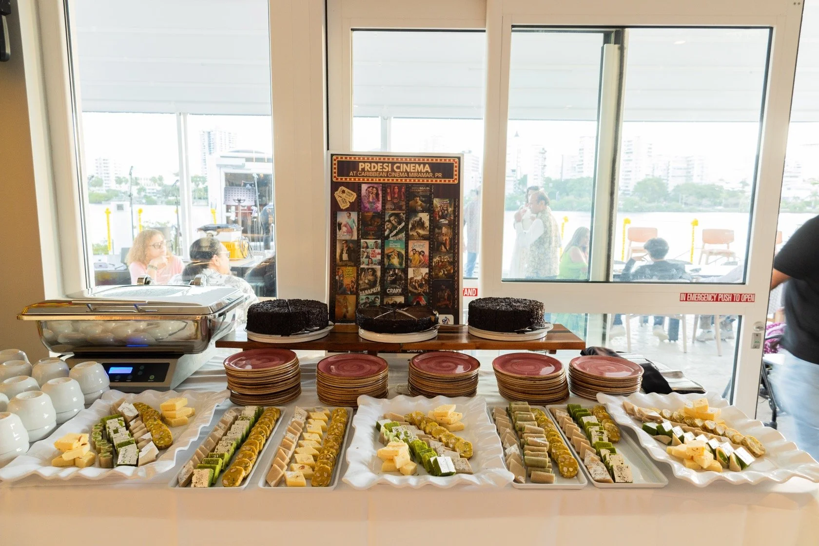 Dessert table with cakes, cheese, and savory snacks at a buffet, with a window and people outside