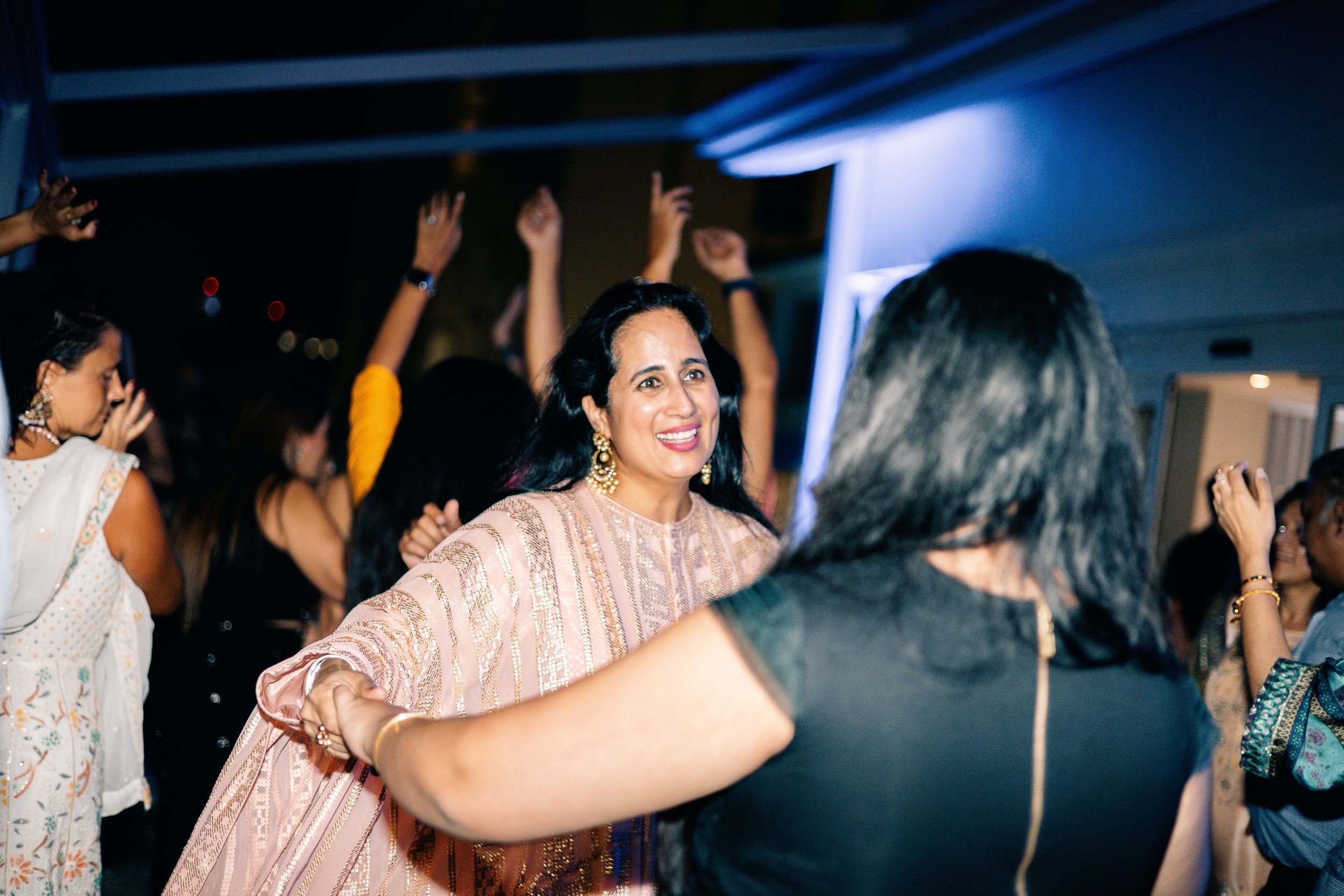 Women dancing and celebrating at a joyful event, with one woman in the center wearing traditional attire and jewelry.
