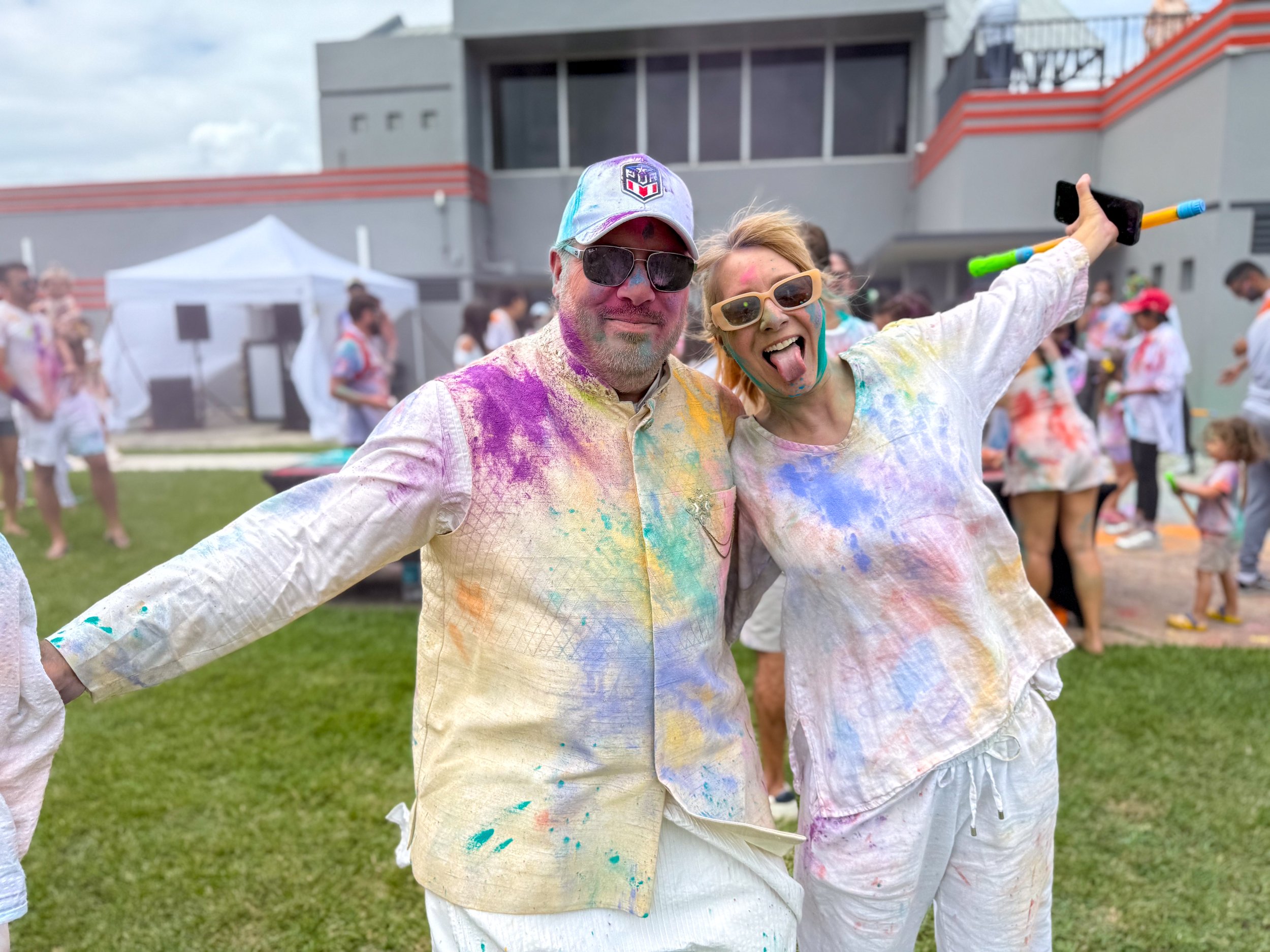 Man and woman covered in colorful powder at a festival, smiling and posing with arms around each other.