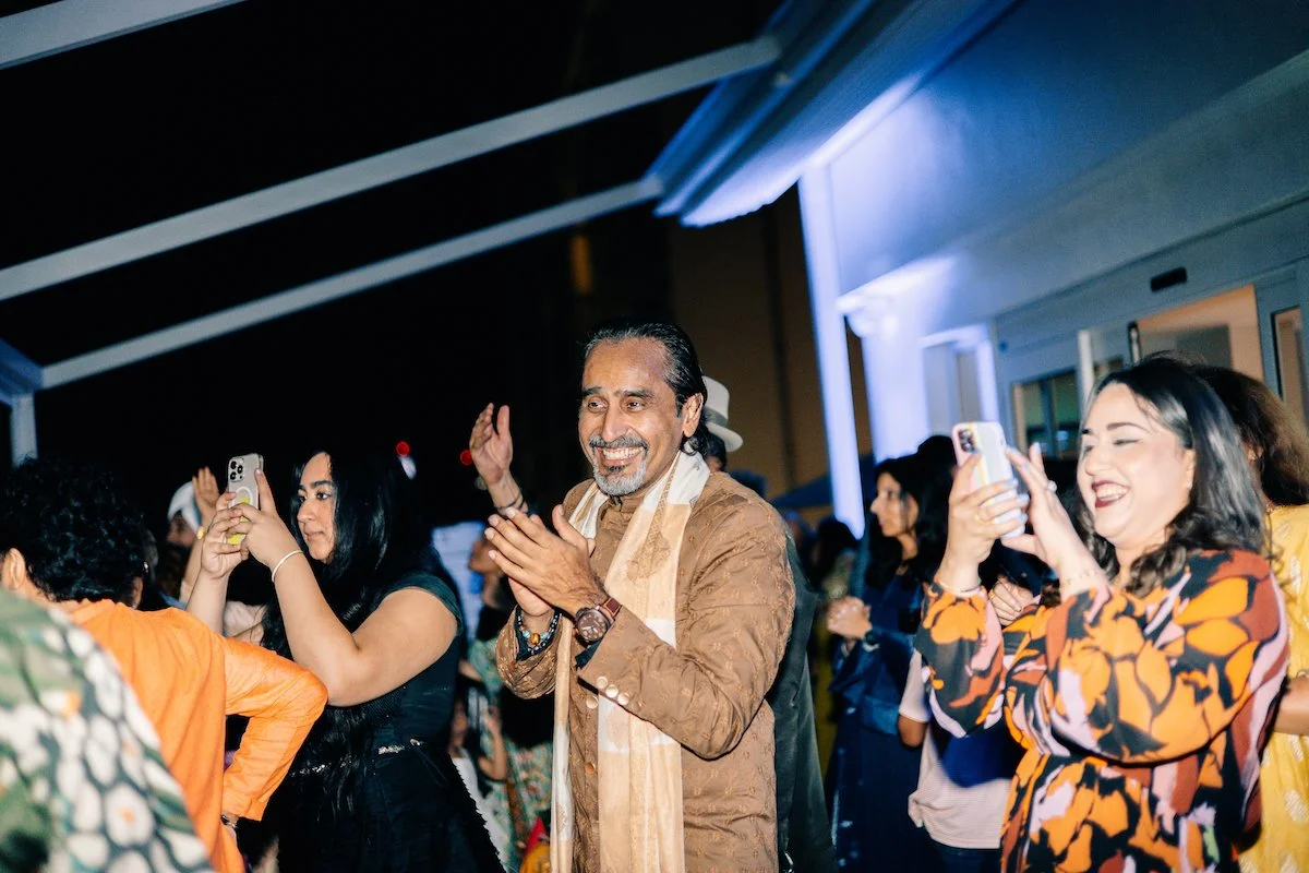 Group of people celebrating at an outdoor event at night, one man clapping, others taking photos, smiling and enjoying the moment.