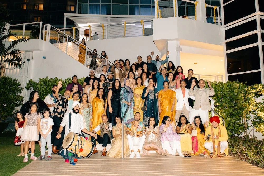 Large group of people, including children and adults, gathered on a staircase outside a modern building during nighttime, some dressed in traditional clothing, posing for a communal photo.