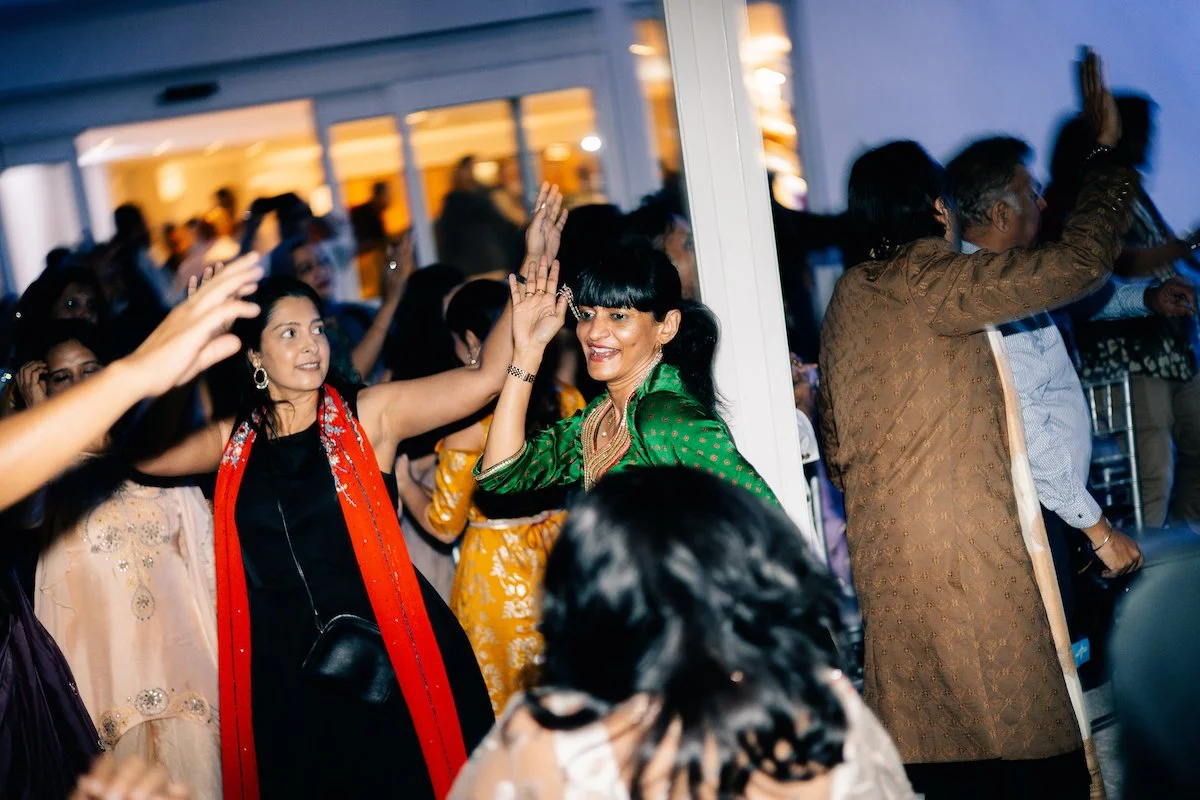 People dancing and celebrating indoors at a party, with some raising their hands and smiling.