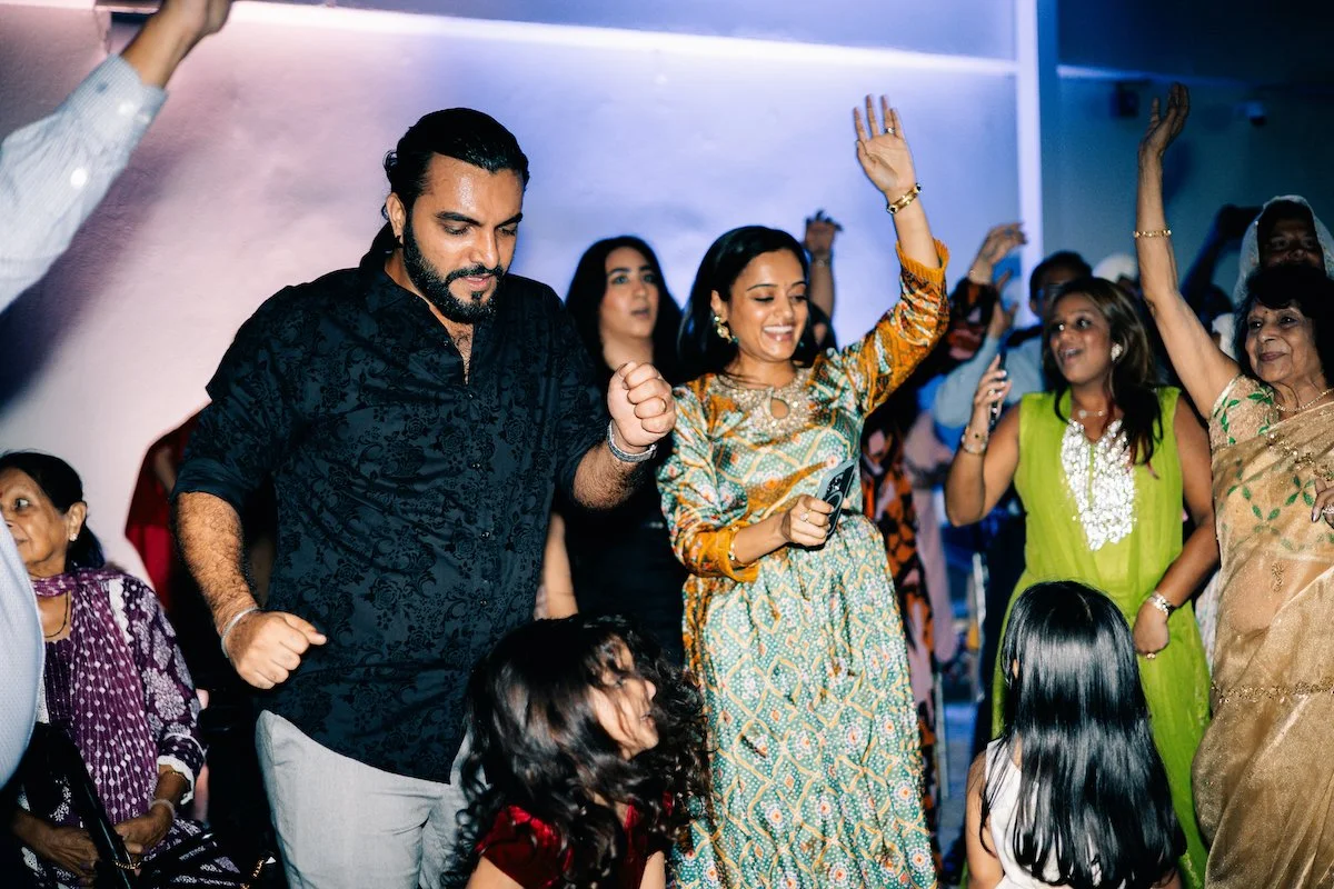 Group of people dancing and celebrating at a party, with some women in colorful traditional Indian attire.