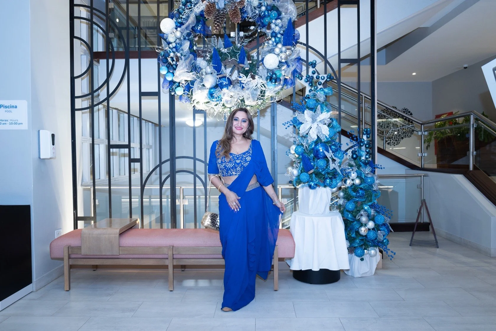 A woman in a blue traditional outfit standing next to large blue and silver Christmas decorations in a hotel lobby.