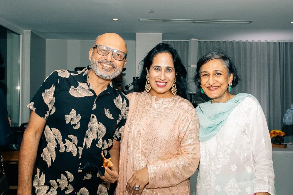 Three smiling people, two women and one man, posing together indoors at a social event.