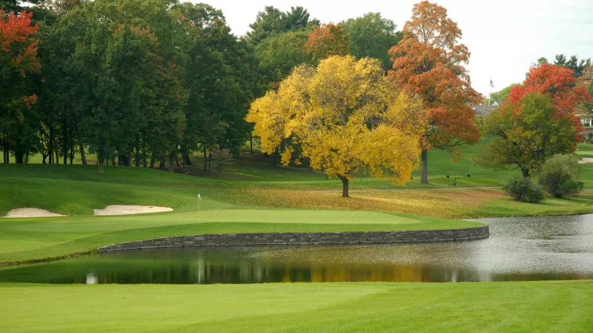 A golf course with green grass, sand traps, water hazard, and colorful autumn trees.